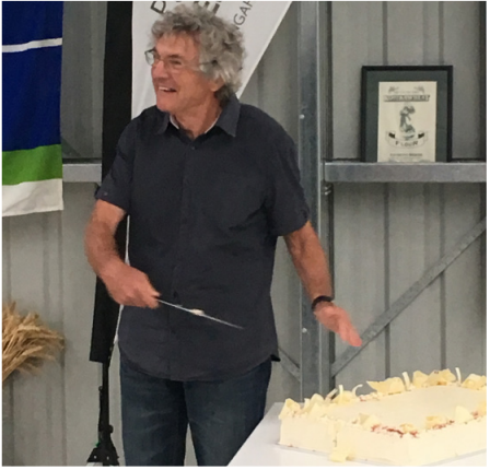 Dr Bill Griffin cuts a large cake with a knife, laughing at something out of shot